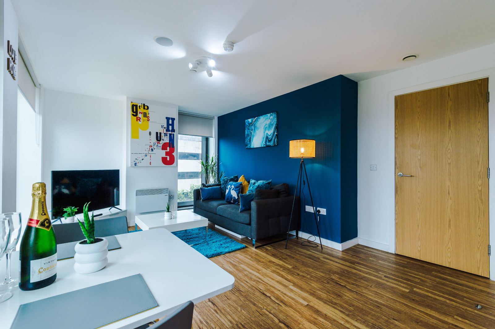 Staged open-plan living room with navy feature wall, floor lamp and dining setup