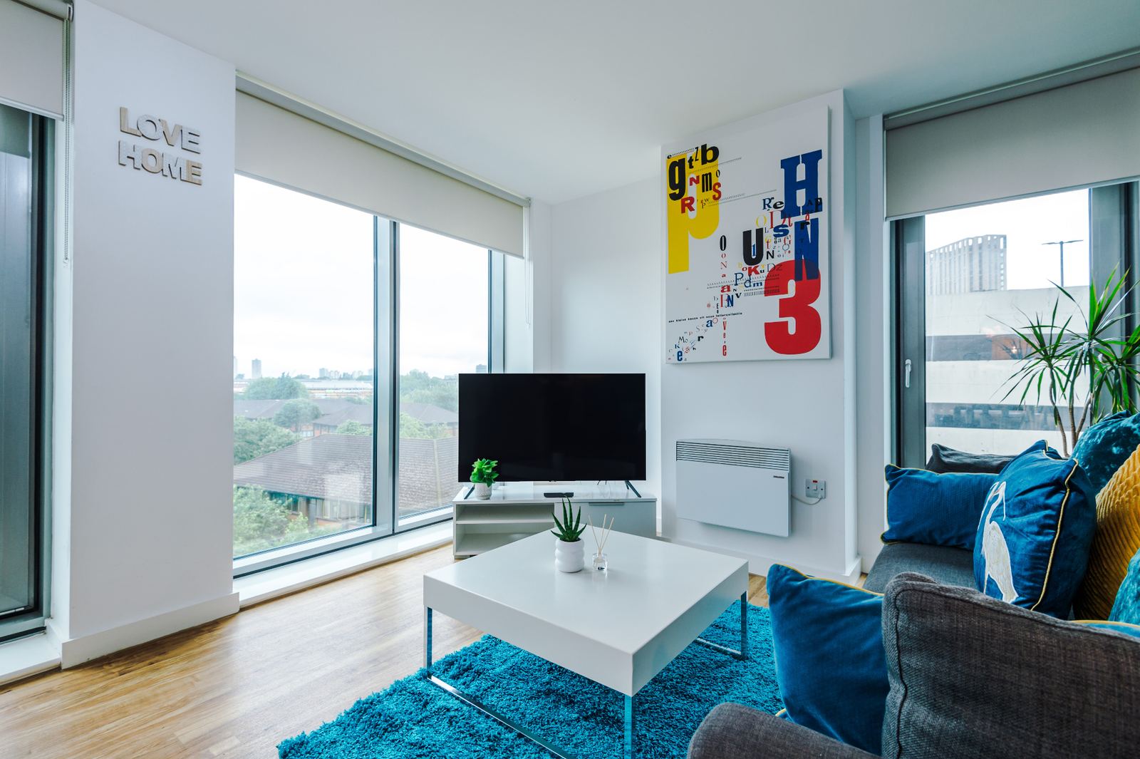 Bright staged living area with blue rug, coffee table and city-view windows