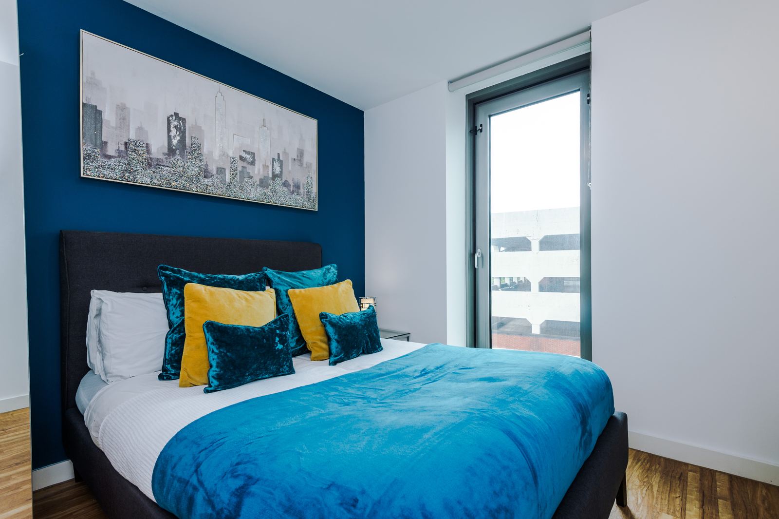 Styled bedroom with blue feature wall, layered cushions and framed city artwork