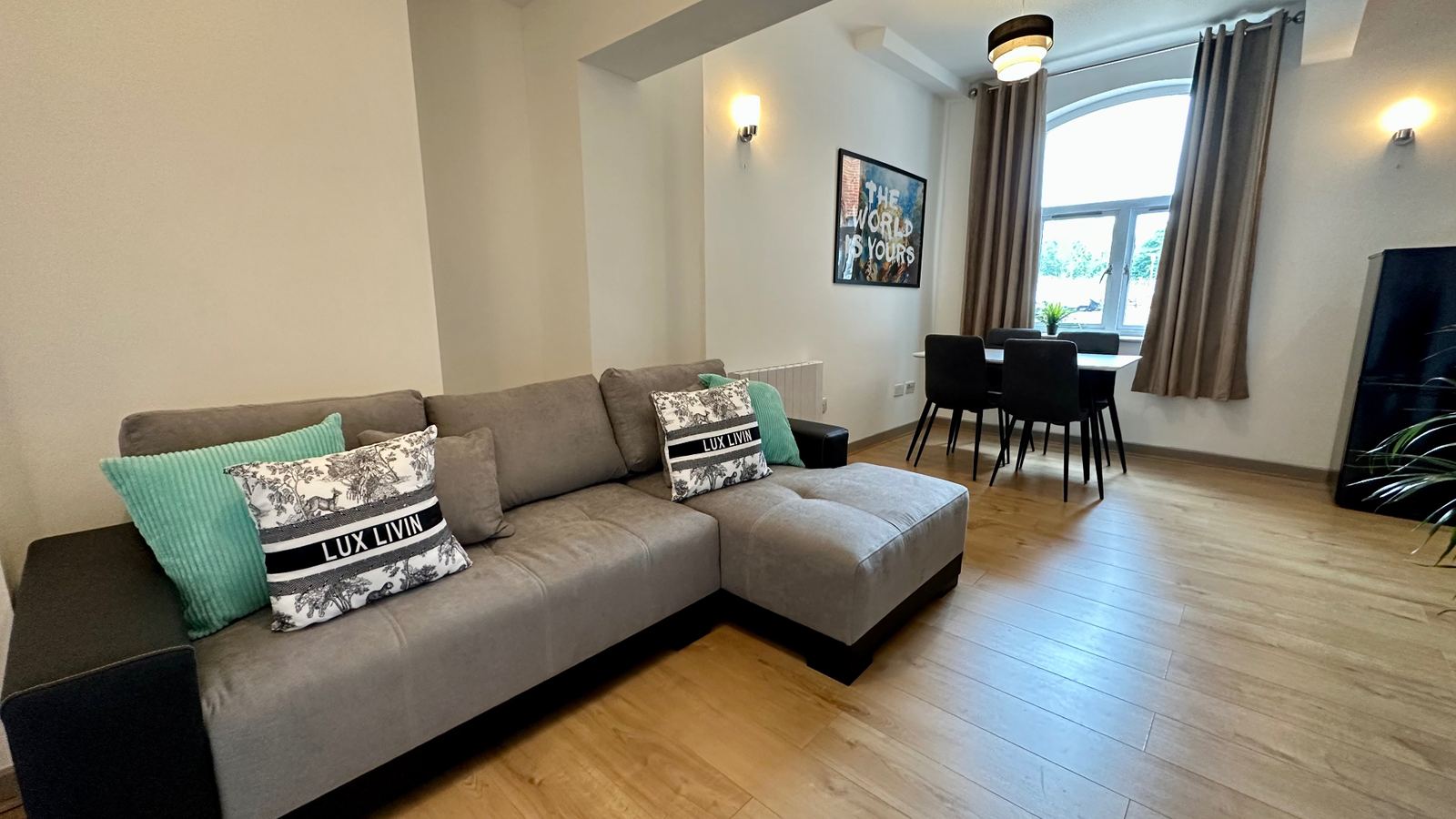 Staged lounge with grey corner sofa, mint cushions and 'The World Is Yours' artwork
