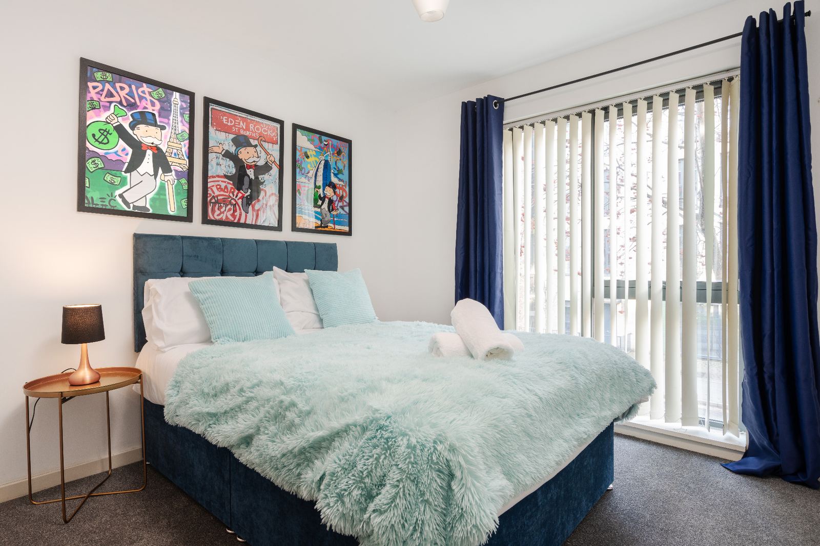 Staged bedroom with navy velvet headboard, pop-art prints and styled bedding