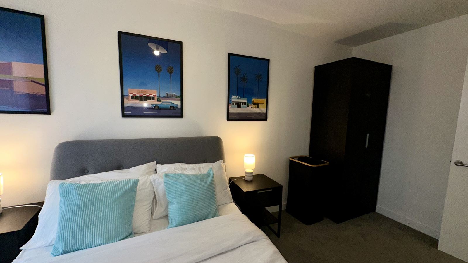 Waterhouse styled bedroom with grey upholstered headboard, framed art and bedside lamp